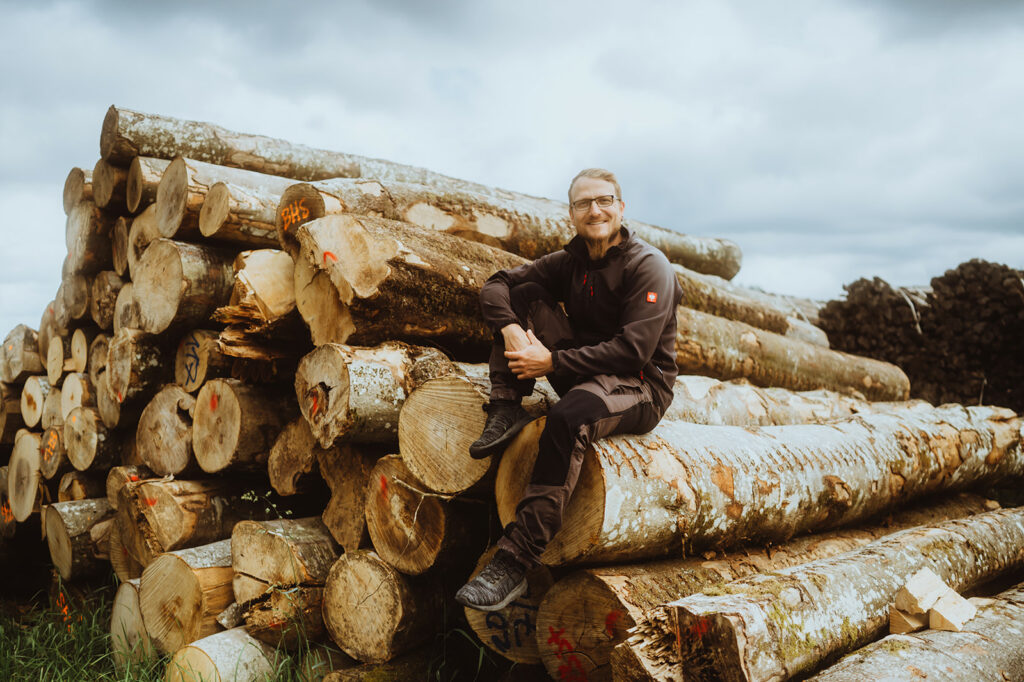 Mann sitzt auf Holzstapel lachend.